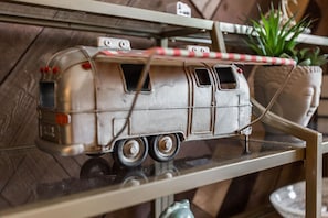 Silver model camper van with a red and white awning, a potted plant, and a decorative head on a shelf.