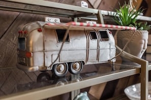 Silver model camper van with a red and white awning, a potted plant, and a decorative head on a shelf.