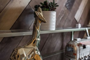 A close-up view of a gold giraffe figurine on a shelf with a potted plant and a miniature camper van in the background.