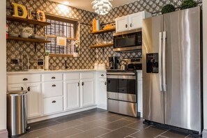 Modern kitchen with white cabinets, stainless steel appliances, patterned wallpaper, and a large chandelier