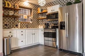 Modern kitchen with white cabinets, stainless steel appliances, patterned wallpaper, and a large chandelier