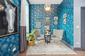 Compact room, blue accent wall, framed artwork, with two chairs.