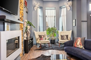 Close view of the living room with a fireplace, a plush couch, two chairs, and a television, all resting on warm hardwood floor.