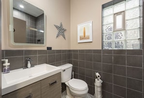 Bathroom with gray tile walls, a white sink and toilet, a large mirror, and a block glass window.