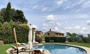 Fienile (farmhouse) and big sky viewed from the pool, loungers in foreground