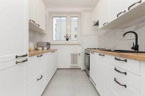 A sleek, all-white kitchen with modern appliances, ample storage, and a large window providing daylight.
