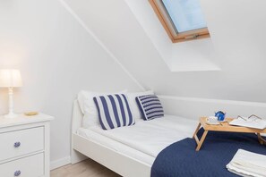 A bright bedroom under a sloped ceiling with a blue-striped pillow on a white bed, creating a seaside ambiance.

