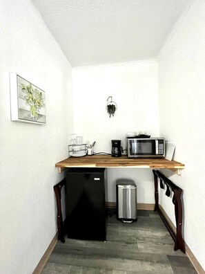 Kitchenette with coffee maker, microwave, mini fridge, coffee cup, wine glasses and silverwares.