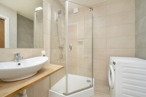 A contemporary bathroom with a glass shower, white sink, and beige tiles.