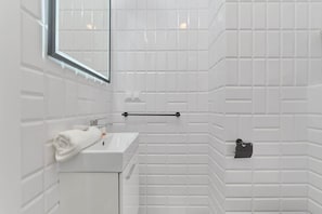 A modern bathroom with white textured tiles, a minimalist sink, and a large mirror, offering a clean and bright atmosphere.