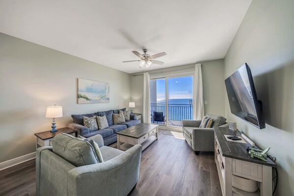 The living room offers ample, comfortable seating, a flat screen television, gulf views, and doors leading to the unit's private balcony.