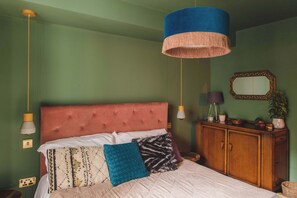 A calming green bedroom with a pink upholstered bed, wooden furnishings, and soft lighting.