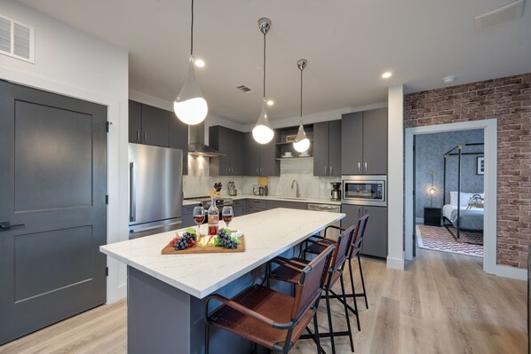 Fully equipped kitchen stocked with basic cooking essentials, stainless steel appliances, and breakfast bar seating, all connected to the dining area.