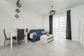 A spacious living room featuring a dining area with a white table and chairs, complemented by blue accents.