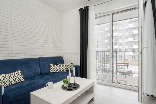 A modern living room with a blue corner sofa, white coffee table, and balcony access, creating a bright and airy atmosphere.