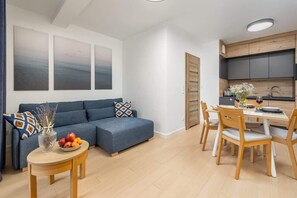 An open-concept living and dining area with a blue sofa, wooden dining table, and large windows, allowing ample natural light.

