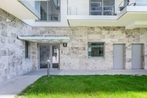 The building's entrance with a clean, minimalist facade and well-maintained green space, showcasing the contemporary architecture.

