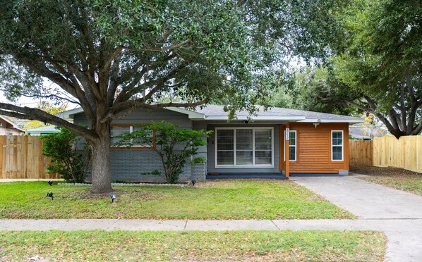 This elegant home features a charming front porch, surrounded by lush greenery, offering a welcoming entrance. Accessible for all, the porch requires just one small step to enter, combining style with convenience.