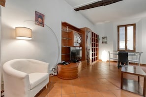 Living room with Smart HD TV, sofa bed, crystal table, leather chairs, library.