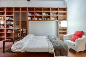 Living room with Smart HD TV, sofa bed, crystal table, leather chairs, library.