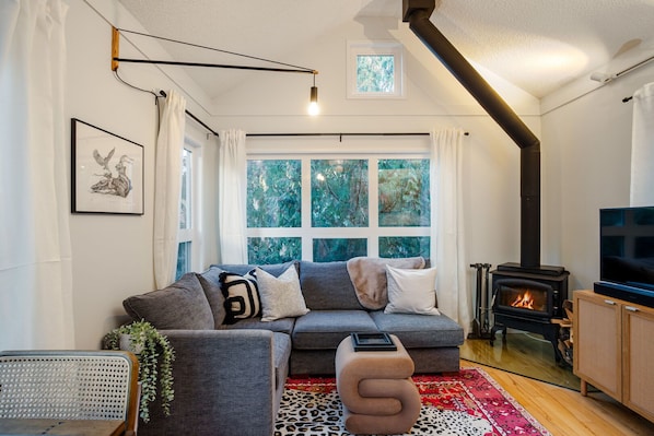 Cozy and inviting living space featuring a plush L-shaped couch, TV, and a charming wood-burning fireplace.