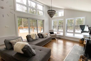 Living room. Seating area is surrounded by large windows with forest view.