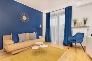 A stylish living room with blue accent wall, beige sofa, and yellow rug, offering a modern and vibrant space for relaxation.