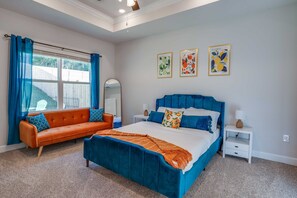 Bedroom with carpeted floors, queen bed, cozy sofa, and window with curtains