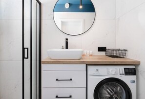 A compact bathroom with a round mirror, washing machine, and a sink with modern fixtures, combining functionality with style.
