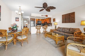A vibrant tropical-themed living area with bamboo furniture, a ceiling fan, and a view of the open kitchen. The perfect blend of comfort and beach-inspired decor.