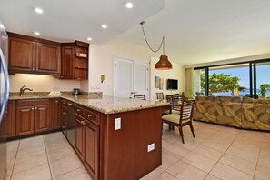 Spacious kitchen with granite countertops flowing into a bright living area with ocean views, perfect for family gatherings and meal preparation.