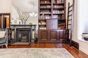 The living room oozes charm and character with a fireplace, a dark wooden bookcase, and a ladder to reach the collection.