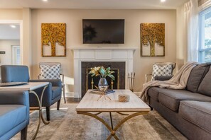 Our living area features a large flat-screen TV mounted on the wall, a cozy fireplace beneath it, and two extra chairs for additional seating. It's the perfect spot for family and friends to come together.