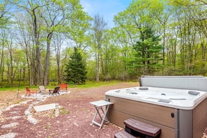 A serene backyard setting featuring a bubbling hot tub and a fire pit surrounded by Adirondack chairs. The perfect spot to unwind under the stars.