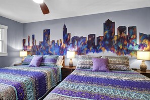 This bedroom features a custom Raleigh skyline mural and two plush queen-sized beds. 