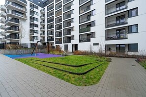 An exterior view of the apartment complex with well-maintained greenery, paved pathways, and contemporary architectural design.
