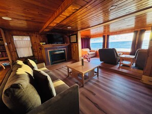 Cozy living room with ocean views, wood walls, sleeper sofa, TV, and fireplace.
