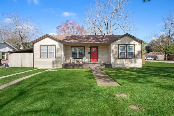 Our house with a lovely green lawn and a striking red door, making it a delightful sight to come home to every day  