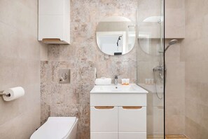 Stylish bathroom with beige marble tiles, a glass shower cabin, and a white vanity with a circular mirror, offering a luxurious feel.