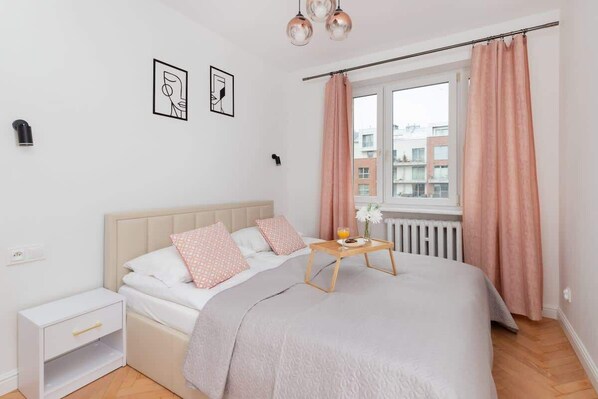 Elegant bedroom with soft pink curtains, a beige bed with pastel pillows, and a golden bedside table, creating a cozy and romantic atmosphere.