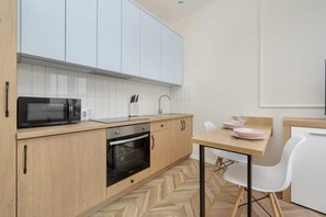 A contemporary kitchen with light wooden cabinets, a black oven, a microwave, and a small dining area for two.
