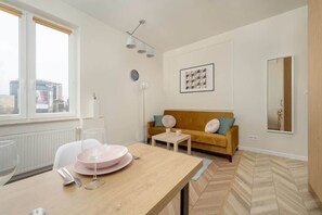 A dining table set with pink plates, positioned near a mustard sofa in a spacious living room with large windows.
