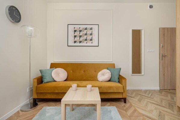 A bright living area with a mustard-colored sofa, white walls, a modern wall lamp, and a minimalist coffee table.
