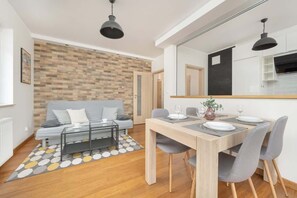 A dining area with a wooden table, grey chairs, and a brick accent wall, giving a modern yet rustic charm to the space.
