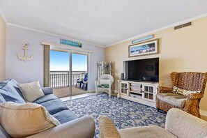 The living room is adorned with comfortable furnishings, a queen sofa sleeper, large smart TV, and sliders to the oceanfront balcony