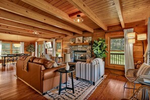 Gorgeous log cabin with fireplace, open concept living and dining spaces, TV, dining room table with space for 6, and plenty of seating.