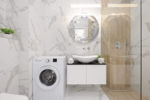 A chic bathroom with marble-style tiles, a glass shower enclosure, a washing machine, and a minimalist vanity unit, blending luxury with practicality.

