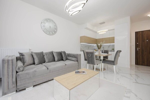 A stylish living room with a plush gray sofa, a glass coffee table, and a modern chandelier, creating an elegant and cozy atmosphere.

