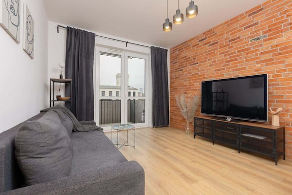 A modern living room with a grey sectional sofa, brick accent wall, and a wall-mounted TV, combining industrial and contemporary design elements.