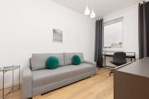 A cozy seating area with a grey sofa, green accent cushions, and a desk, creating a functional and stylish workspace.

